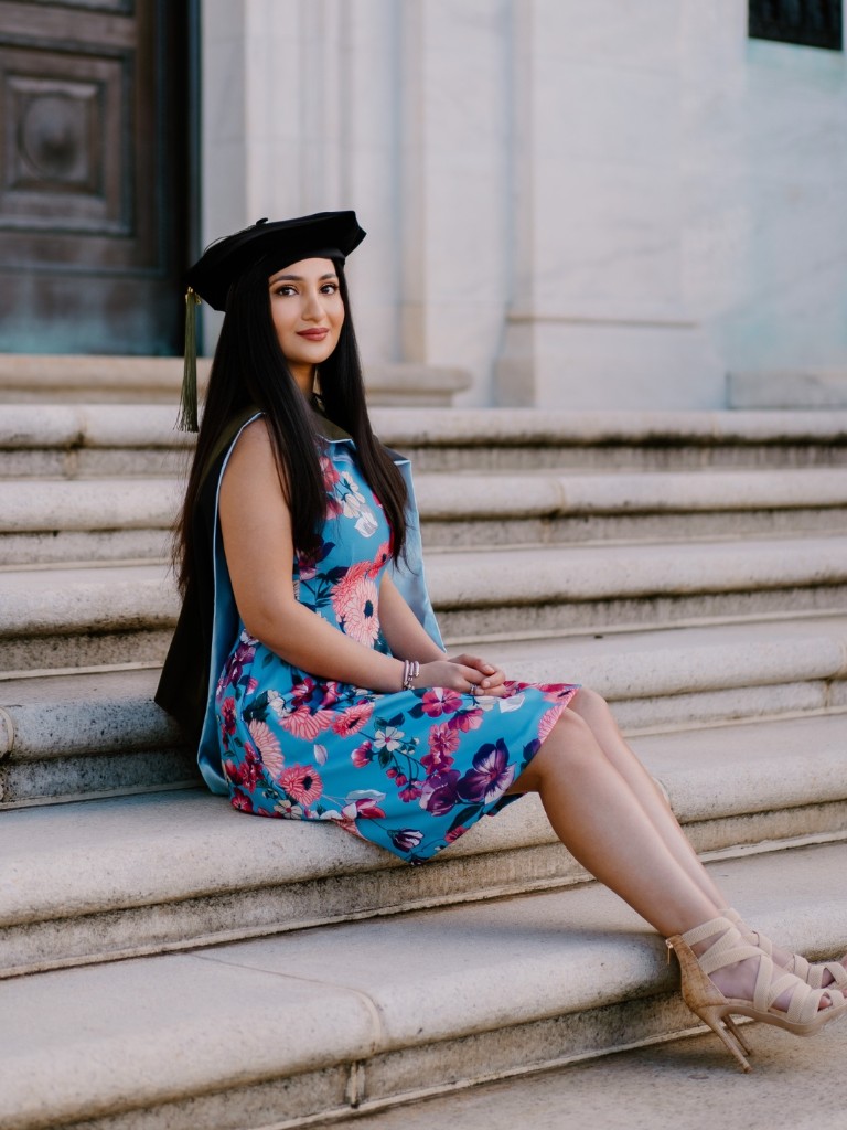 Dr. Sarah, PharmD, sitting on the steps in graduation cap and gown